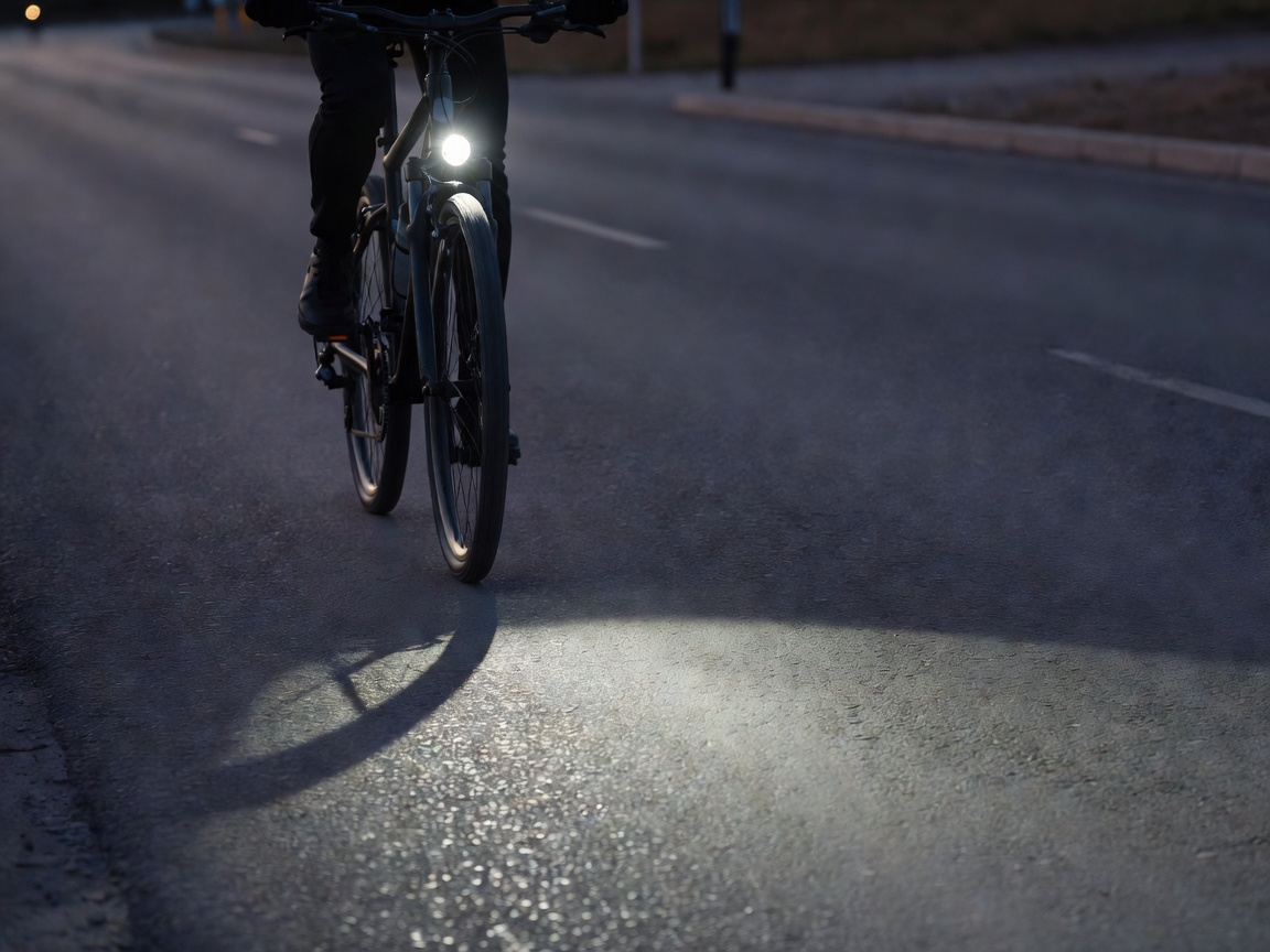Professional realistic photograph: Real front bicycle light emitting a focused beam onto a realistic road ahead. Genuine lighting conditions, no AI artifacts.